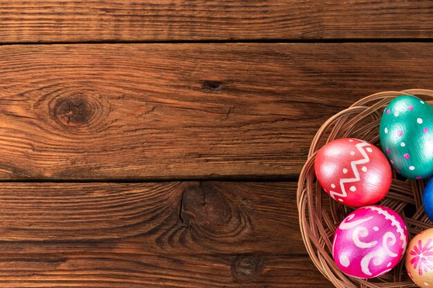 Five easter eggs trendy colored deep blue, green, orange, magenta and golden decorated in basket on old wooden table.