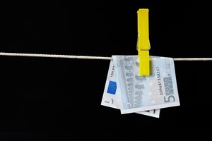 Five euro banknote fastened with a clothespin is dried on a clothesline on dark background