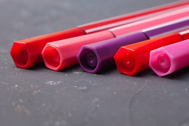 Photo five markers or pens in pink, purple, pink on a black.