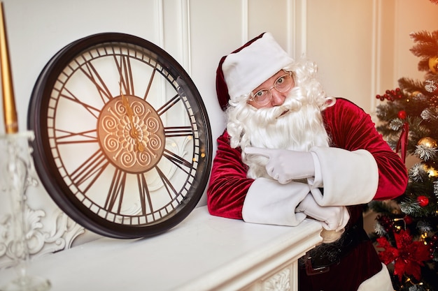 Foto cinque minuti a capodanno o mezzanotte di natale. babbo natale felice mostra sull'orologio