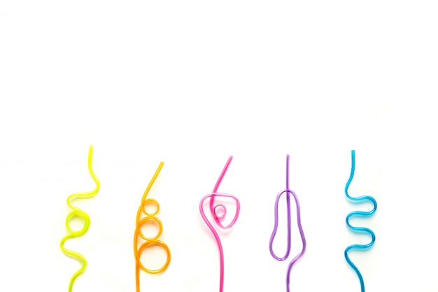 Five multi-colored tubes for cocktails lie in a row on a white background. Multi-colored straws for drinks twisted in different shapes