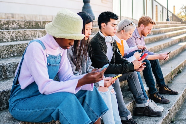 Cinque amici multirazziali che usano i loro smartphone seduti all'aperto