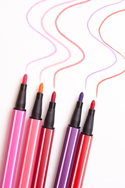 Five open markers or pens in pink, purple, pink on a white