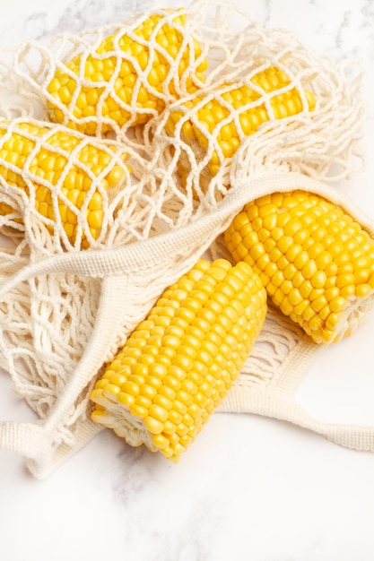 Five pieces of corn in a cotton mesh bag on a white marble kitchen counter in a top view