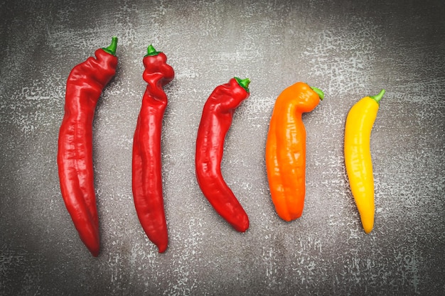 Five pieces of red orange yellow long pepper going down on a dark stone