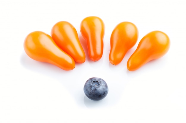 Five small ripe orange grape tomatoes and a single blueberry isolated on white background