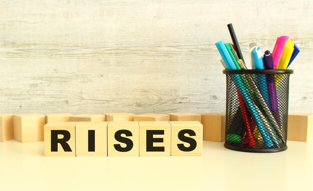 Five stacked wooden cubes with letters RISES on a white desktop on a gray background