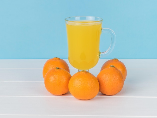 Cinque mandarini e un bicchiere di vetro con succo su un tavolo bianco