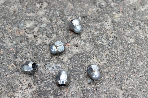 Five wheel nuts securing the wheel to the hub lie on the pavement near the car tire shop while repla...