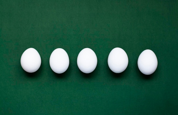 Five white eggs lie on a dark green background