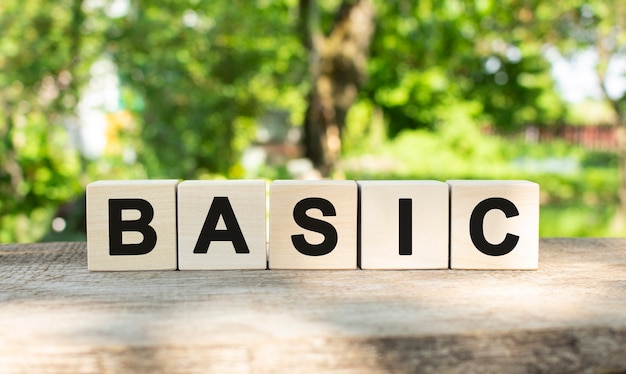 Five wooden blocks lie on a wooden table against the backdrop of a summer garden and create the word BASIC.