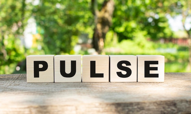 Five wooden blocks lie on a wooden table against the backdrop of a summer garden and create the word PULSE