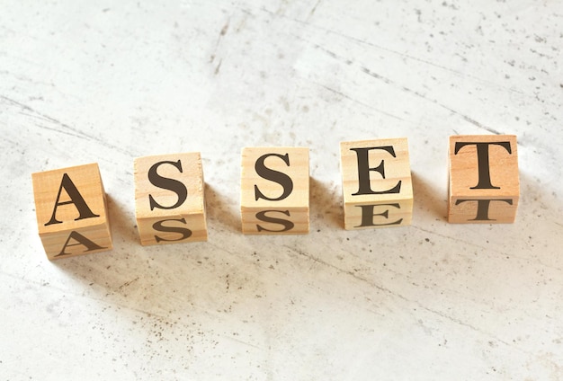 Five wooden cubes with word ASSET on white stone like board, view from above