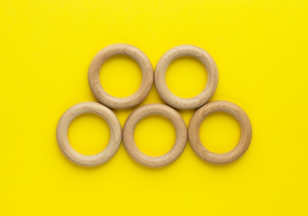 Five wooden rings on yellow background. natural wood baby teether. eco-friendly children toy. top view, flat lay with copy space