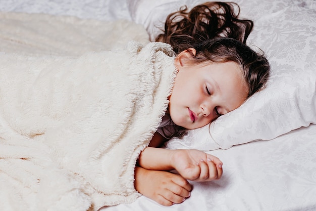 A five-year-old girl sleeps peacefully on an orthopedic pillow, home comfort and warmth, healthy sleep.