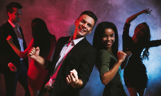 Five young people of different genders and nationalities are dancing together with their hands up in the air, laughing and enjoying themselves