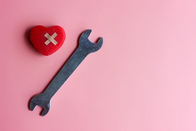 Fix mend a broken heart concept Red heart bandage and spanner on pink background with copy space