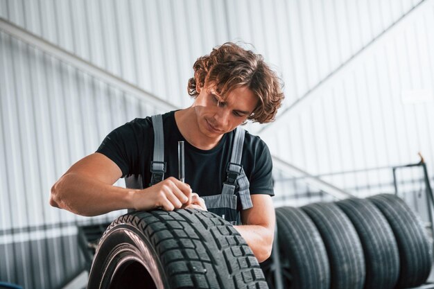 Fixes broken tire Adult man in grey colored uniform works in the automobile salon