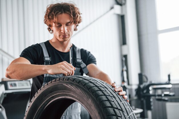 Fixes broken tire Adult man in grey colored uniform works in the automobile salon