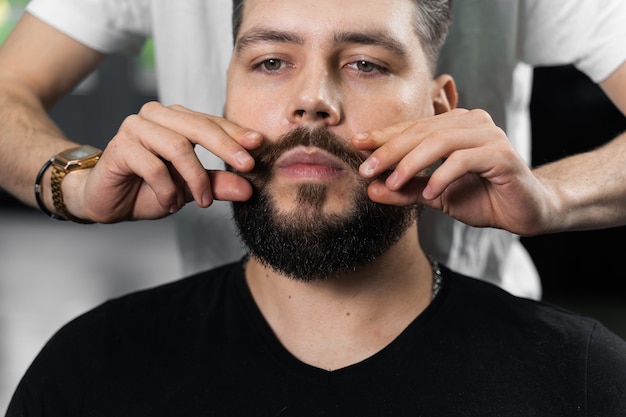 Fixing the shape of mustache with wax. The result of a haircut in a barbershop.