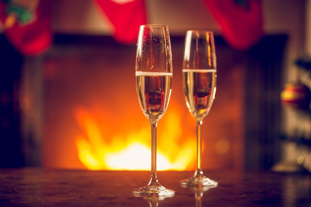 暖炉の前のクリスマステーブルにグラス2杯の発泡性シャンパン