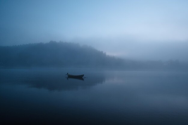 Photo fjord with a small boat on blue foggy morning