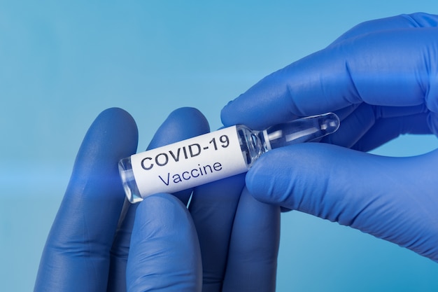 Flacon met kuur Covid-19. De arts, de verpleegster of de wetenschapper die blauwe handschoenen indienen houdt een vaccincoronavirus.