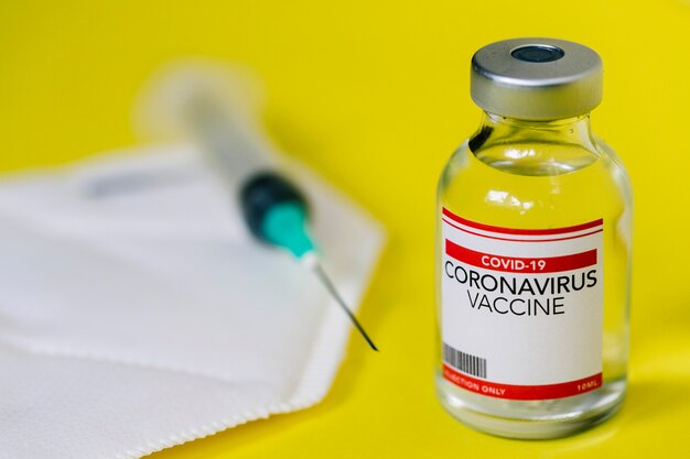 Flacon met vaccin tegen coronavirus covid-19 en spuit op een beschermend gezichtsmasker. gezondheidszorg en medisch concept