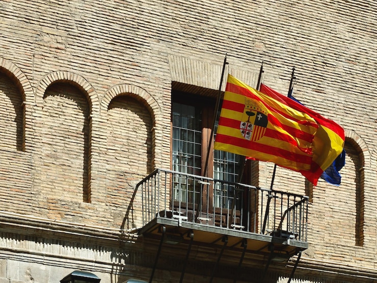 アラゴン コミュニティ スペインと EU の旗がサラゴサのダウンタウンの公共市役所のバルコニーに手を振っています。 スペインの紋章