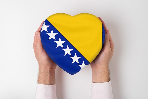 Bandiera della bosnia ed erzegovina su una scatola a forma di cuore in mani maschili.