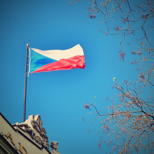 The flag of the Czech Republic on a building with blue sky and the sun in the background.