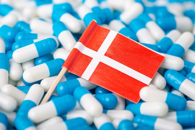 Flag of Denmark on piles of pills. Concept of epidemic in Denmark country