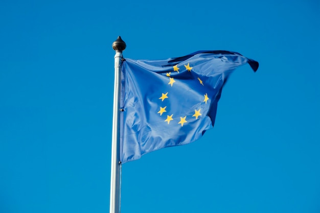 Flag of european union waving in the wind on flagpole against blue sky on sunny day