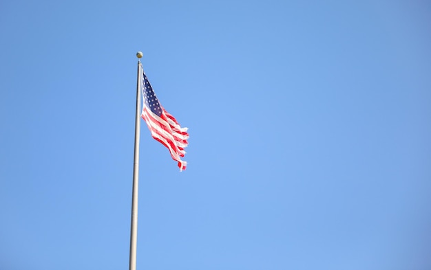 A flag on a flag pole with a blue sky in the background.