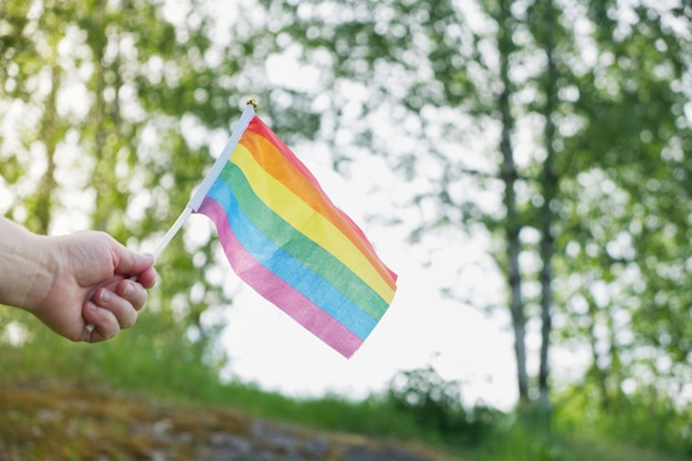 잔디와 나무의 배경에 있는 lgbt 커뮤니티의 깃발, 여성의 손에 든 깃발