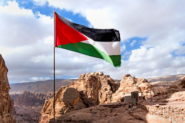 Flag of Palestine flutters in wind on top of a mountain against a cloudy blue sky