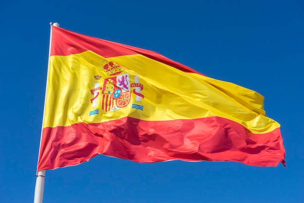 Flag of Spain in the wind on a mast on a sunny day. blue sky background