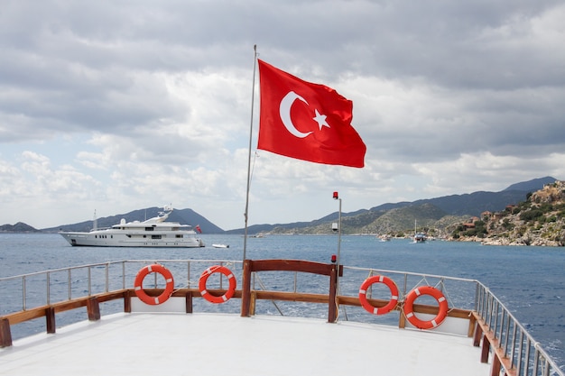 Flag of Turkey on a ship at sea near mountains and a luxury yacht