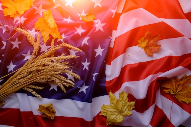 Flag United States America strewn with yellowed autumn maple leaves and bunch wheat ears