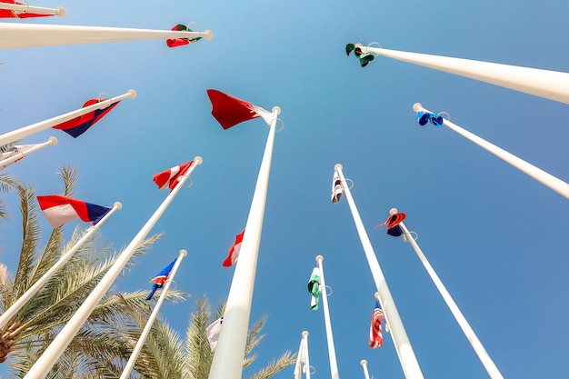 Flags of different countries of world flutters in wind background of blue sky Bottom up view