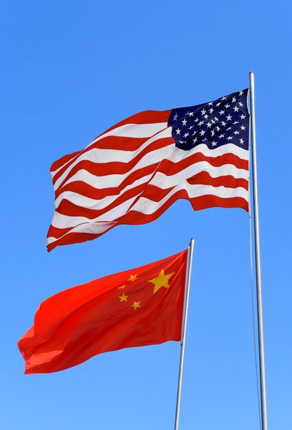 Flags of USA and China are flying in the wind against the blue sky