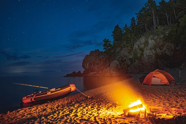 Foto la fiamma di un fuoco di campo sullo sfondo del lago baikal estivo notturno con una barca e una tenda