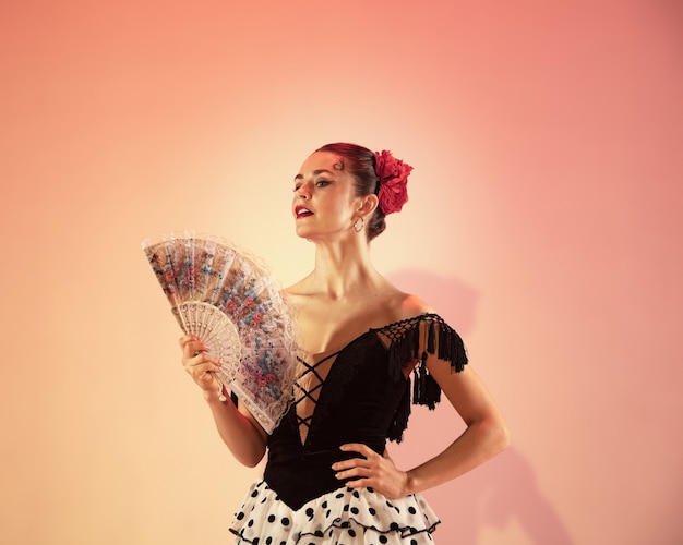 Photo flamenco dancer. spain woman gypsy with red rose and spanish hand fan posing and dancing at studio. passionate spanish temperament and passion in dance. human emotions concept