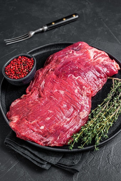 Flank or flap raw beef steak on plate with thyme. Black background. Top view.