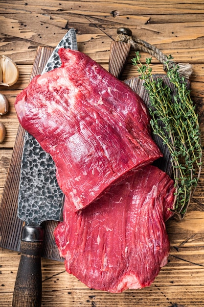 Photo flank raw beef steaks on a butcher cutting board with knife. wooden background. top view.