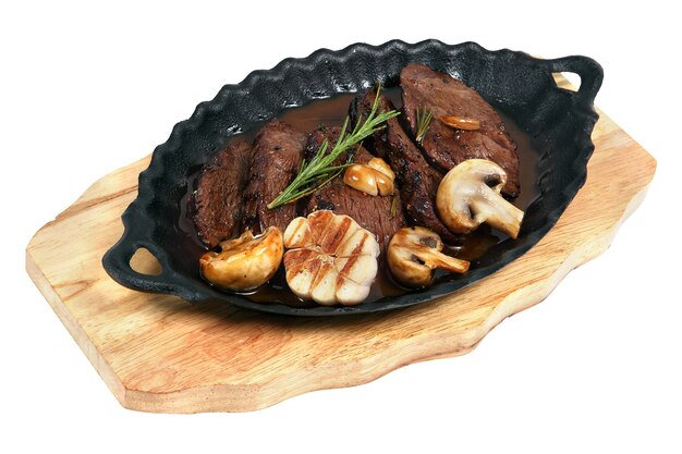 Flank Steak with mushrooms cooked in cast iron dish oval, standing on wooden board, studio shot, isolated on white background.