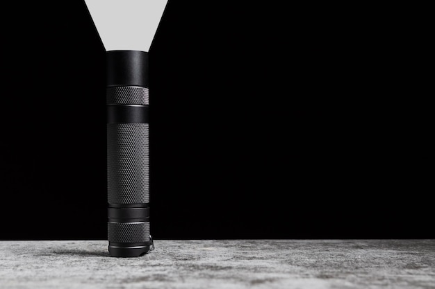 Flashlight stands on a table with beam of light upwards and copy space