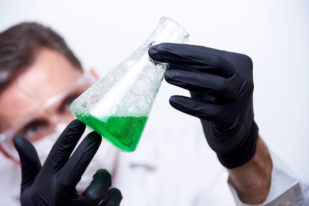 A flask with a green liquid and bubbles in the hands of a young man.