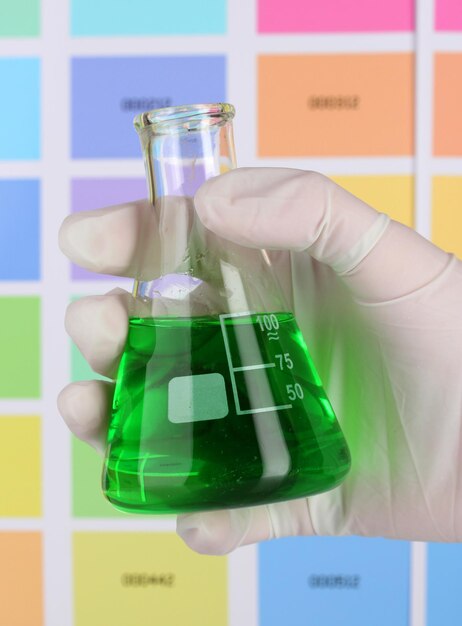 Flask with green liquid in hand on color samples background
