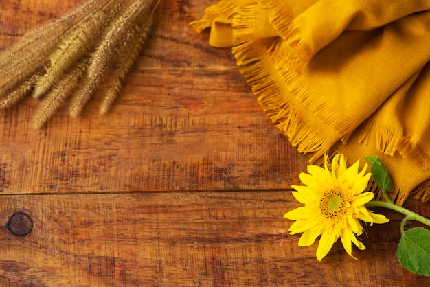 Flat composition with yellow knitted scarf, wheat spikelets and sunflower on a wooden table. Cozy autumn or the concept of winter rest. Place for text, frame, top view, copy space, layout